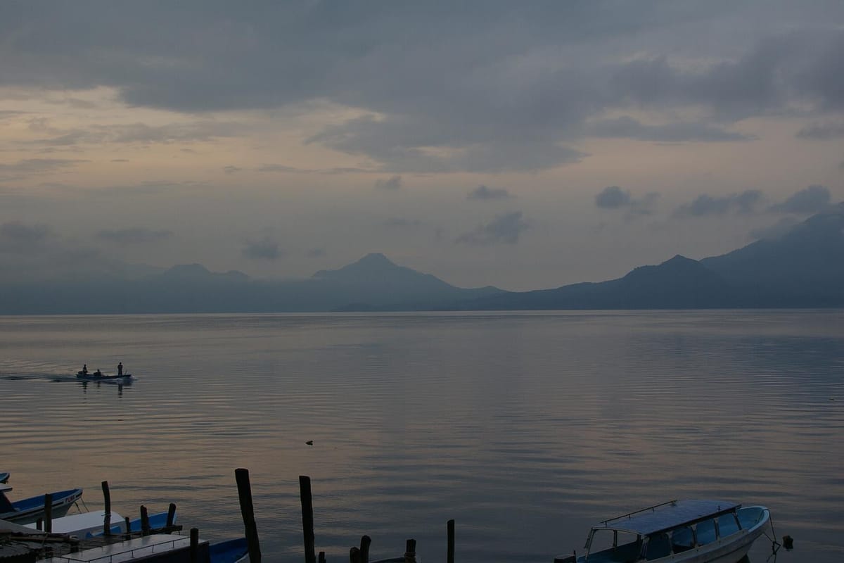 Dawn over Lago de Atitlán, with volcanic ridges on the far shore and small passenger launches moored in the foreground